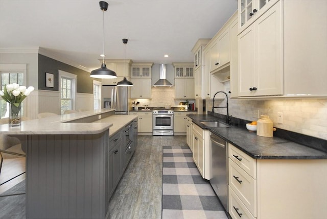 kitchen featuring a wainscoted wall, a breakfast bar, a sink, stainless steel appliances, and wall chimney exhaust hood