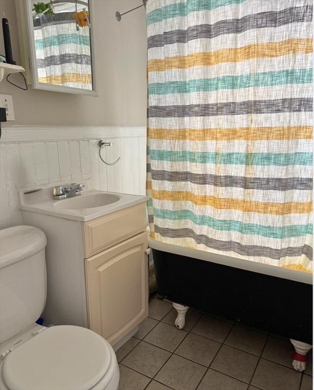 full bathroom with tile patterned flooring, vanity, toilet, shower / bathtub combination with curtain, and a wainscoted wall
