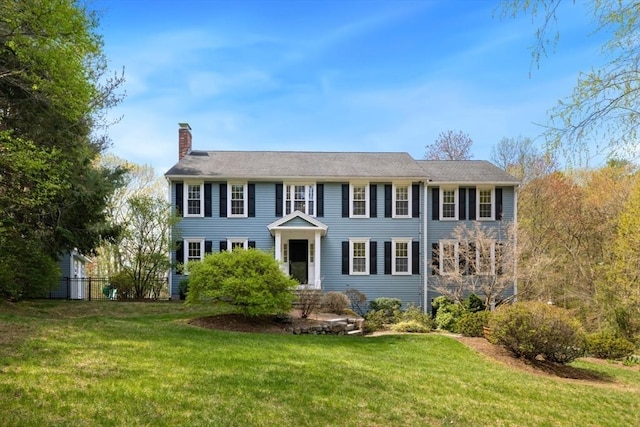 colonial inspired home with fence, a chimney, and a front yard