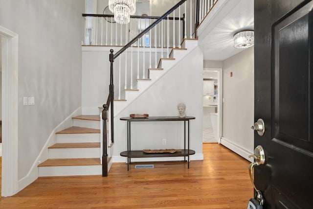 entrance foyer featuring a baseboard heating unit, baseboards, a chandelier, wood finished floors, and stairway