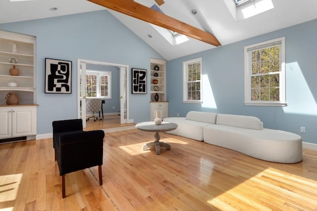 living area with high vaulted ceiling, a skylight, light wood-type flooring, baseboards, and built in shelves