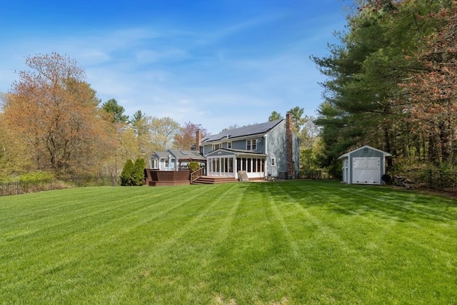 view of yard featuring a sunroom, fence, a wooden deck, an outdoor structure, and a shed