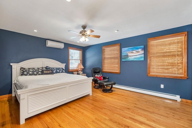 bedroom featuring a baseboard heating unit, an AC wall unit, baseboards, and wood finished floors