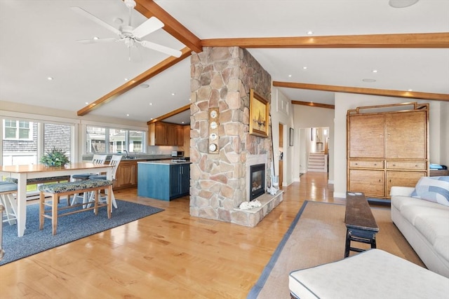 living area with light wood-style flooring, ceiling fan, and a stone fireplace