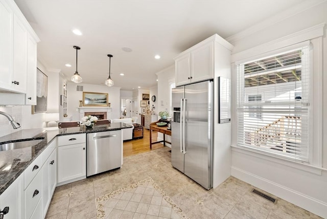 kitchen with sink, white cabinetry, stainless steel appliances, decorative light fixtures, and dark stone counters