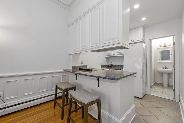 227 Marlborough St Unit 4, Boston, MA 02116 - kitchen featuring freestanding refrigerator, a kitchen bar, white cabinets, a baseboard heating unit, and dark stone counters