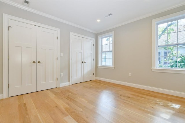 unfurnished bedroom featuring multiple closets, light wood-style flooring, multiple windows, crown molding, and recessed lighting
