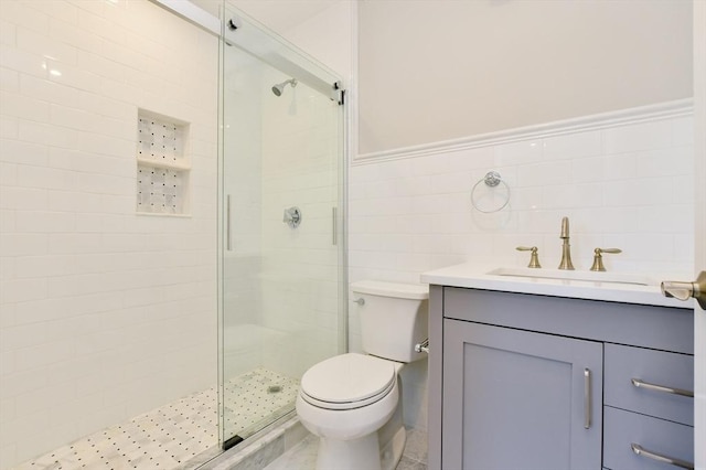 bathroom with a shower stall, tile walls, vanity, toilet, and a wainscoted wall