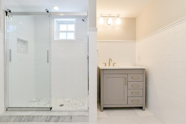 bathroom with a shower stall, tile walls, a wainscoted wall, tile patterned floors, and vanity