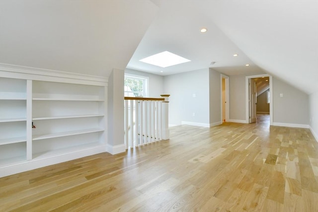 bonus room with a skylight, vaulted ceiling, light wood-style floors, built in shelves, and recessed lighting