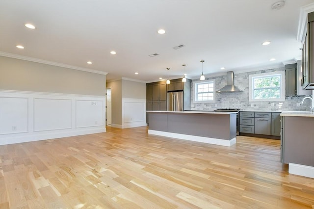 kitchen with high quality fridge, wall chimney range hood, crown molding, a center island, and tasteful backsplash
