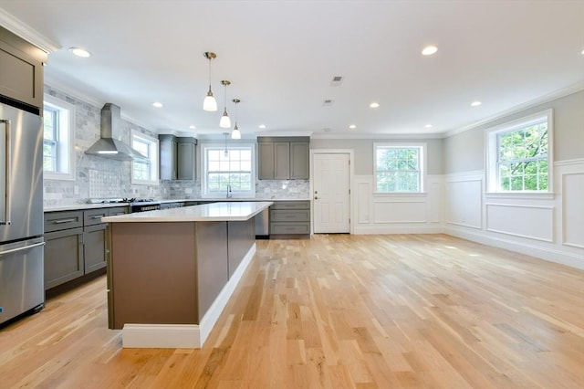 kitchen featuring wall chimney exhaust hood, gray cabinetry, stainless steel appliances, crown molding, and light countertops