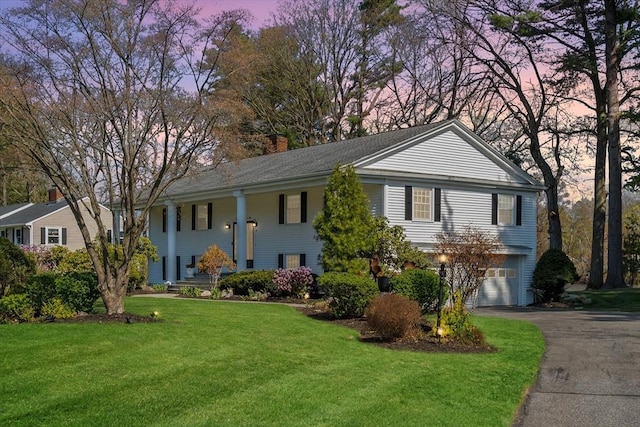 view of front of home featuring a garage, driveway, a chimney, a lawn, and a porch