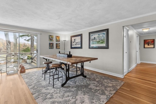 dining room with baseboards, wood finished floors, ornamental molding, a textured ceiling, and attic access