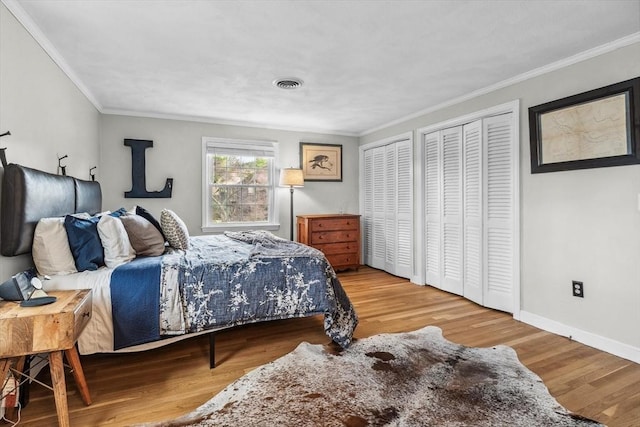 bedroom with two closets, wood finished floors, crown molding, and baseboards