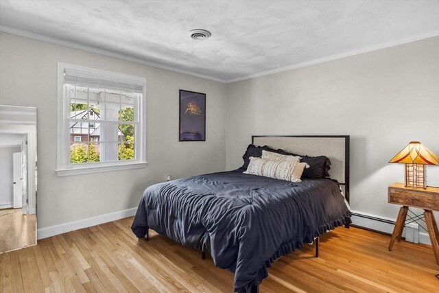 bedroom with a baseboard heating unit, wood finished floors, baseboards, and ornamental molding