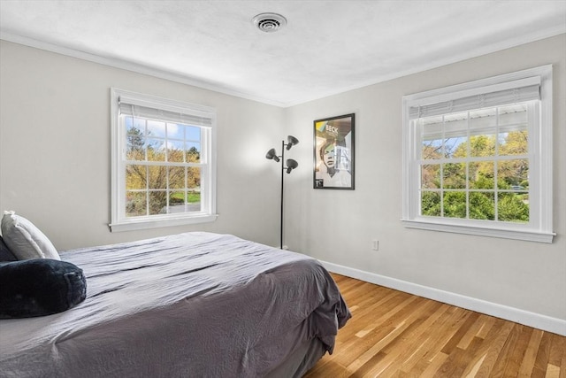 bedroom with crown molding, baseboards, light wood-style flooring, and multiple windows