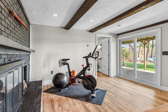 workout area featuring baseboards, wood finished floors, a textured wall, a brick fireplace, and recessed lighting