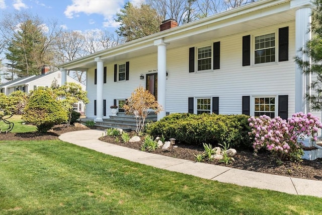 bi-level home featuring a chimney, covered porch, and a front lawn