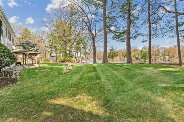 view of grassy yard with a deck with water view and stairs