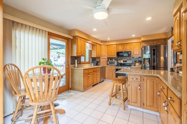 kitchen with appliances with stainless steel finishes, a ceiling fan, decorative backsplash, light tile patterned flooring, and a kitchen bar