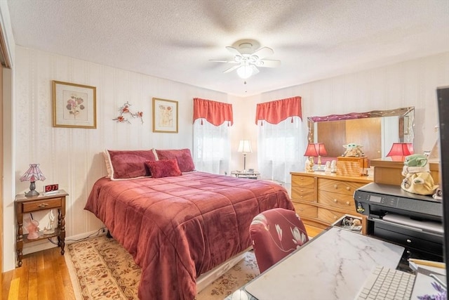 bedroom featuring wallpapered walls, light wood-type flooring, a textured ceiling, and a ceiling fan