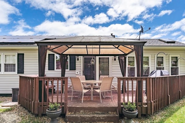 rear view of house featuring a deck, a gazebo, roof mounted solar panels, and outdoor dining space