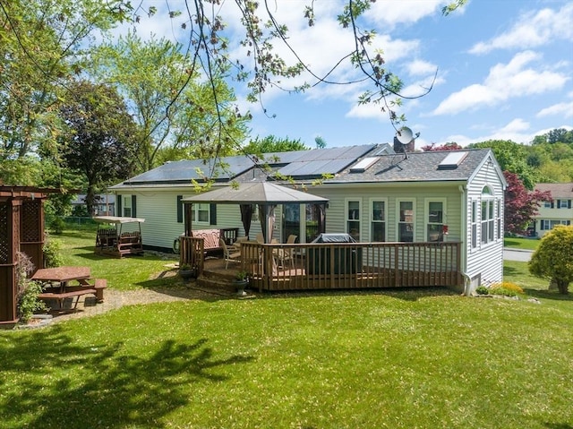 back of house with a wooden deck, a lawn, solar panels, and a shingled roof