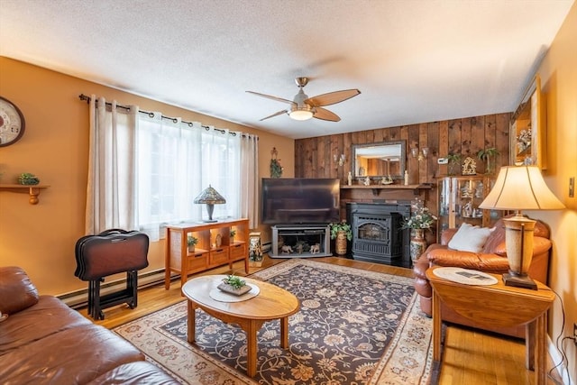 living room featuring wood walls, a ceiling fan, wood finished floors, baseboard heating, and a textured ceiling
