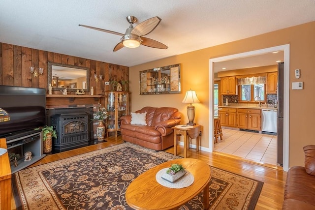 living room featuring ceiling fan, wooden walls, a wood stove, and light wood-style floors