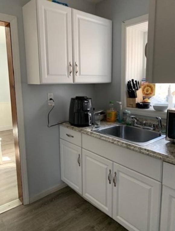 kitchen with dark wood-style floors, baseboards, a sink, and white cabinets