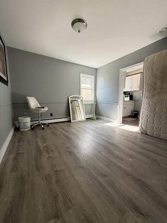 unfurnished bedroom with a baseboard heating unit, dark wood-type flooring, and wainscoting