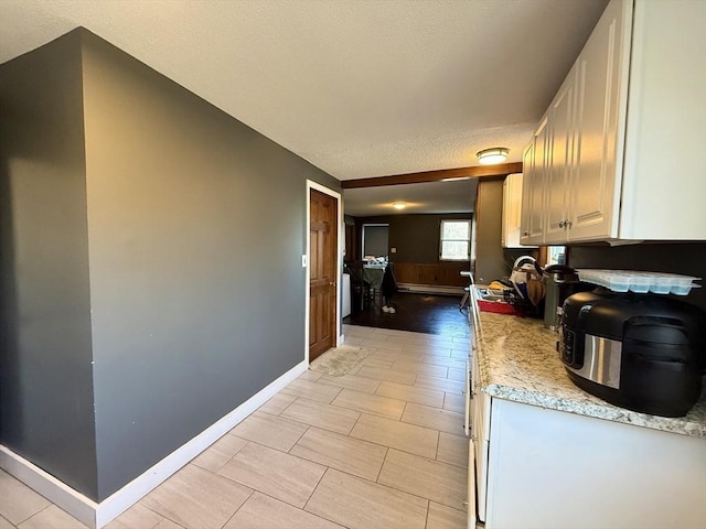 kitchen featuring a baseboard radiator, baseboards, white cabinets, and a textured ceiling