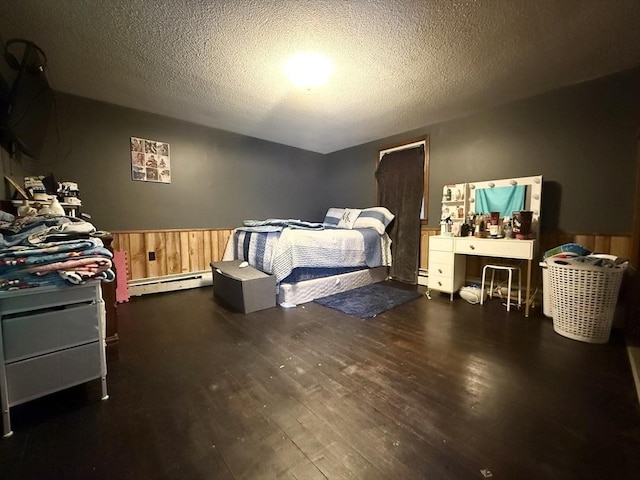 bedroom featuring a wainscoted wall, a textured ceiling, a baseboard heating unit, and wood finished floors