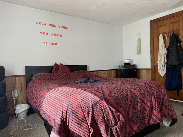 bedroom with carpet, a textured ceiling, wainscoting, and wooden walls