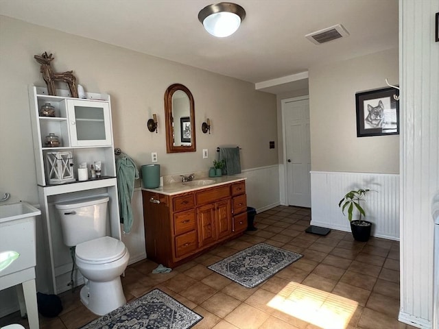 bathroom with a wainscoted wall, visible vents, toilet, vanity, and tile patterned floors