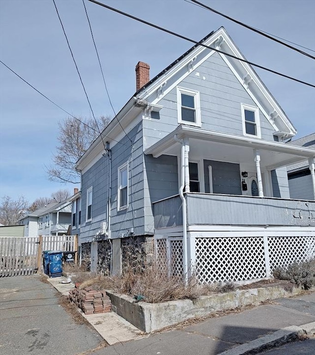 view of front of property with covered porch, a chimney, and fence