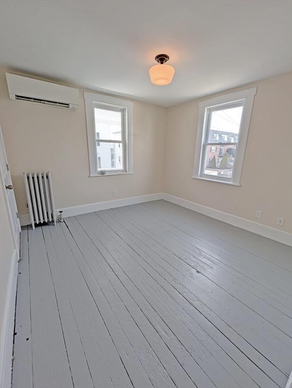 unfurnished room with plenty of natural light, hardwood / wood-style floors, radiator heating unit, and a wall unit AC