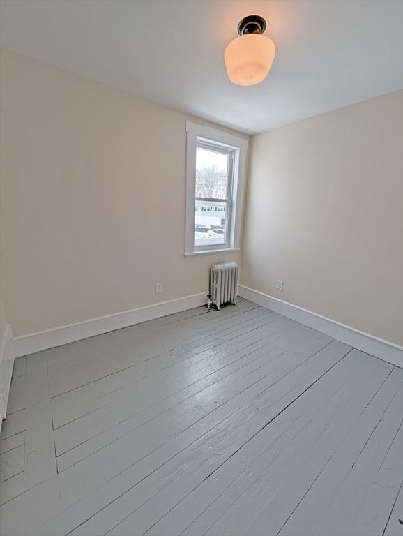 empty room featuring radiator, wood finished floors, and baseboards