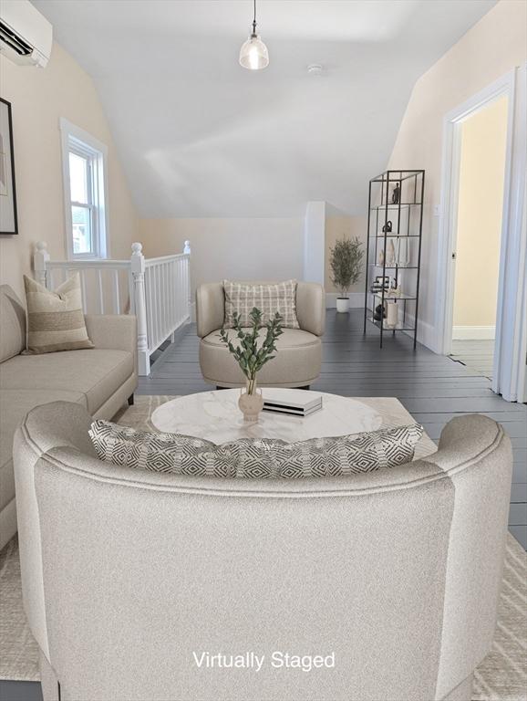 living room featuring baseboards, lofted ceiling, wood finished floors, and a wall unit AC