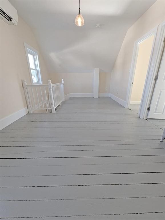 additional living space featuring baseboards, lofted ceiling, light wood-style floors, and a wall unit AC