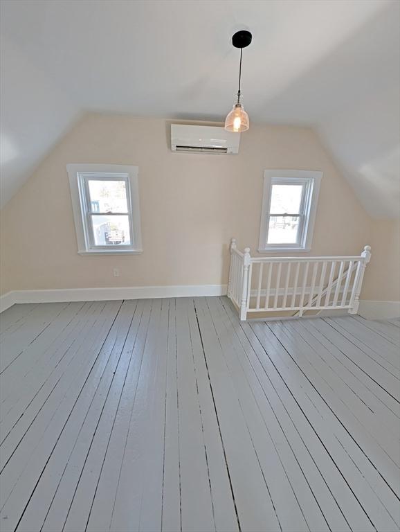 bonus room featuring baseboards, wood-type flooring, lofted ceiling, and a wall mounted AC