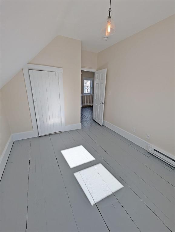 additional living space with a baseboard radiator, baseboards, light wood-style floors, and vaulted ceiling