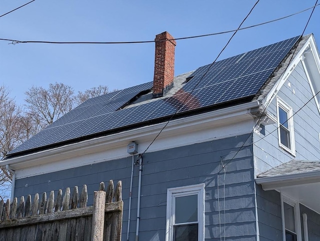 view of home's exterior with roof mounted solar panels, a chimney, and a shingled roof