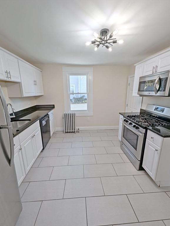 kitchen featuring a sink, appliances with stainless steel finishes, white cabinets, and radiator heating unit