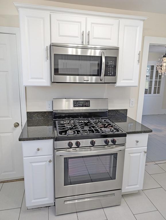 kitchen with light tile patterned floors, dark stone counters, appliances with stainless steel finishes, and white cabinets