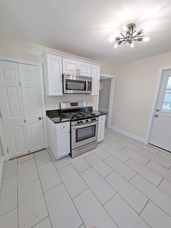 kitchen featuring baseboards, white cabinets, appliances with stainless steel finishes, dark countertops, and a chandelier