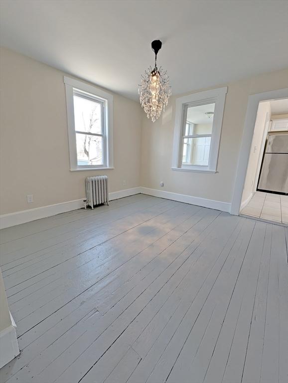 unfurnished room featuring a notable chandelier, radiator, baseboards, and hardwood / wood-style floors