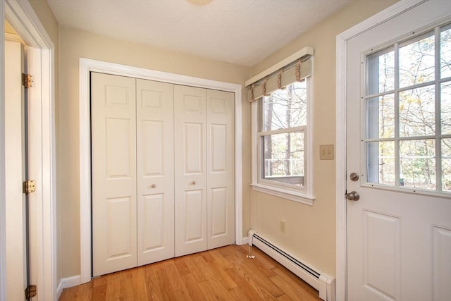 doorway to outside with light wood finished floors, a baseboard radiator, baseboards, and a textured ceiling