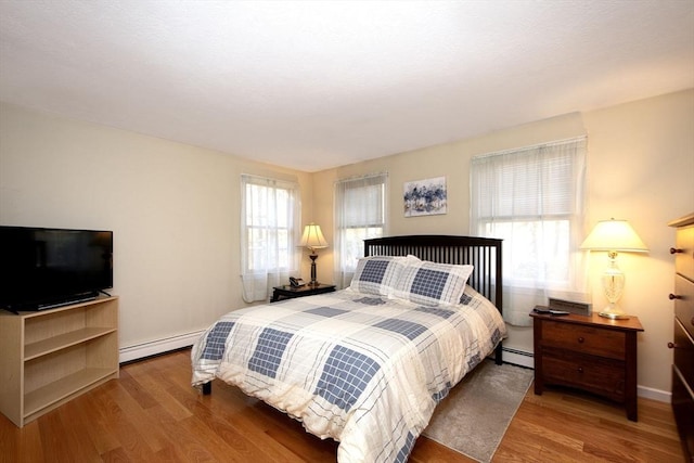 bedroom featuring baseboards, a baseboard heating unit, baseboard heating, and wood finished floors